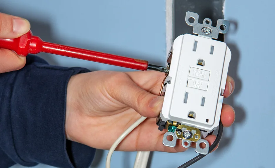 Electrician wiring a white GFCI outlet with an insulated screwdriver